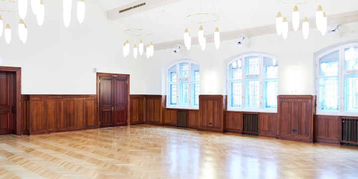 Blick in die Ecke des Johanna-Stirnemann-Saals im Volkshaus mit halbhoher Holzvertäfelung, zwei Holz-Türen & 3 Buntglasfenstern