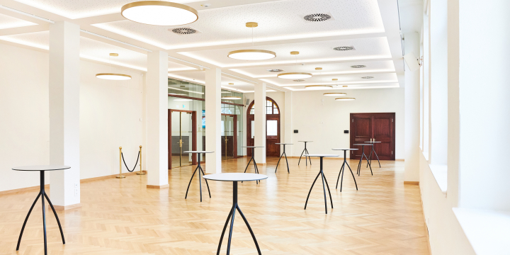 Blick in den hellen Carl-Zeiss-Saal im Volkshaus Jena mit Säulen, die den Raum trennen und auf der rechten Seite Stehtischen.  ©JenaKultur, Karoline Krampitz