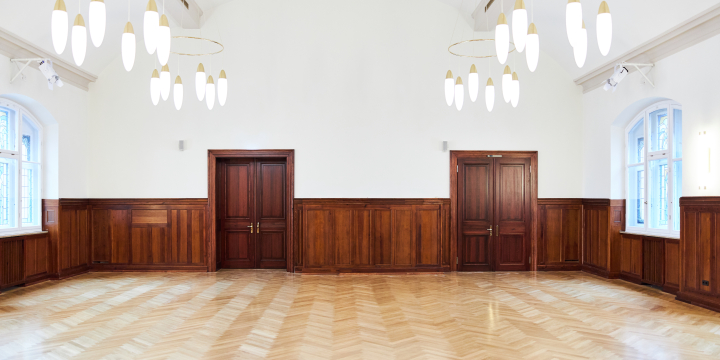 Blick in den Johanna-Stirnemann-Saal im Volkshaus Jena mit zwei Holztüren und zwei Bunstglasfenstern recht und links, welcher halbhoch holzvertäfelt ist  ©JenaKultur, Karoline Krampitz
